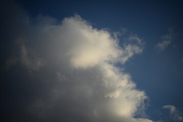 Fototapeta premium rays of the sun through the cirrus clouds against the blue sky, white rainy clouds blue sky illuminated by the rays of the sun, one small cirrus cloud blurred clouds background