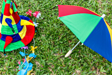 Brazilian carnival items lying on the grass, colorful hat, umbrella and necklace