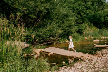 A girl walking on the rocks across the river