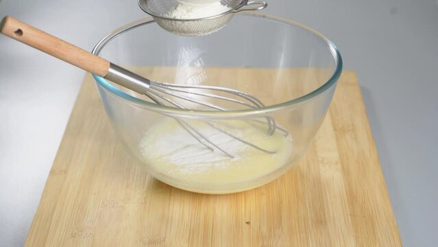 Pour the flour through a sieve into the beaten eggs. Making dough for dessert. High quality 4k footage