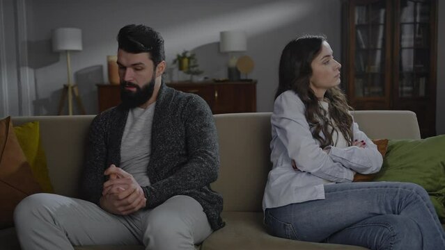 Young bearded man and woman, wife and husband sitting together on the sofa at home after quarrel