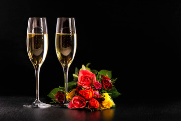 Two glasses of champagne and a bouquet of multi-colored roses on a black background