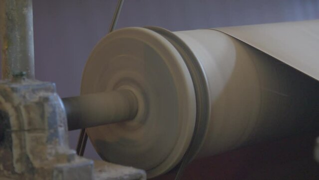 Paper and pulp mill processes a huge sheet of cardboard. An industrial mechanism winds a reel of cardboard into a roll for further box production
