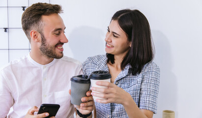 Couple of happy colleagues talking at the office with cups of coffee. Businessman and businesswoman drinking coffee	