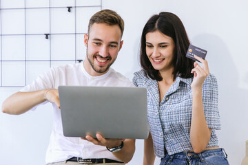 Couple consumer holding credit card and laptop buying online at home. Woman and Man shipping online with credit card in hand. Couple using laptop technology paying credit card shopping online