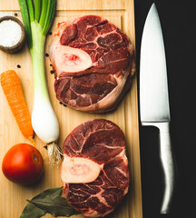 
cut of raw beef osso buco meat, typical Italian with vegetables for milanesa style top view with copy space on wooden chopping block and kitchen knife