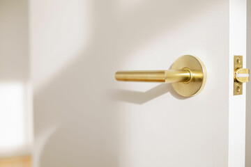 close up of modern gold door handle on white door in sunny room in modern turnkey apartment