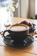 Coffee prepared by a barista in a black cup on a restaurant table. Food accompanying the coffee. Breakfast. Beginning of the day.