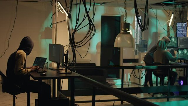 Web criminals making online threats stealing information on multi monitors, breaking into network system with malware. Hackers committing cybercrime and cyberbullying. Tripod shot.