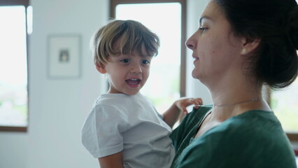 Mother holding child in arms kissing and embracing kid. Candid mom showing love affection to young boy. Authentic real life motherhood relationship