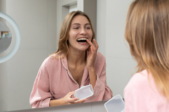 Smiling woman using dental aligner in bathroom