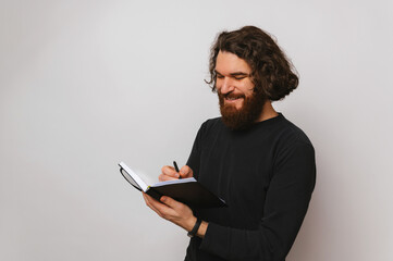 Confident smiling bearded man is writing in his journal the plan of the day.