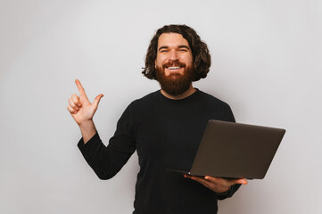 Studio portrait of a young man pointing up while holding opened laptop.