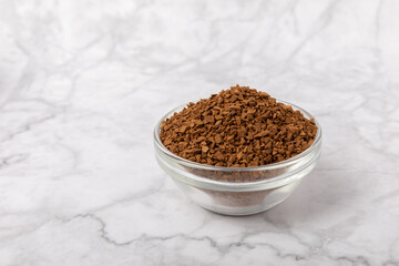 Instant coffee in a glass bowl. Coffee in granules on a white marble background.Energy hot drink....