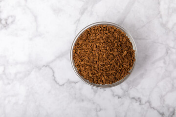 Instant coffee in a glass bowl. Coffee in granules on a white marble background.Energy hot drink....