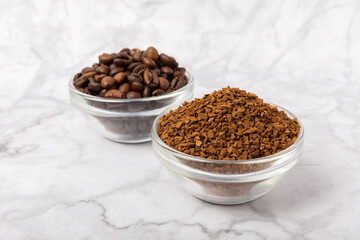 Coffee granules and coffee beans on a white marble background. Instant coffee drink. Energy hot drink. Place for text. Place for copy. Cheerful morning concept.