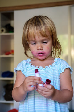 little cute girl makes makeup red lips with lipstick