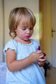 little cute girl makes makeup red lips with lipstick