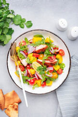 Grilled chicken salad with mango salsa, tomato, cilantro, red onion and lettuce in mexican style, gray table background, top view