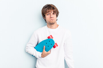Young skater man isolated on blue background shrugs shoulders and open eyes confused.