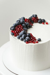 Birthday cake with white cream cheese frosting decorated with fresh blueberries and pomegranate. Elegant summer cake with red and blue berries on the white background