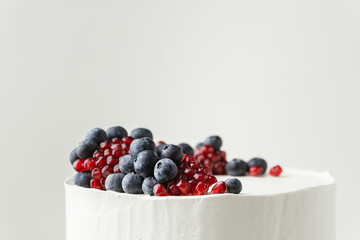 Birthday cake with white cream cheese frosting decorated with fresh blueberries and pomegranate. Elegant summer cake with red and blue berries on the white background