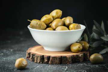 Close up shot of green olives in a white bowl on the wooden stand with olive leaves on a black...