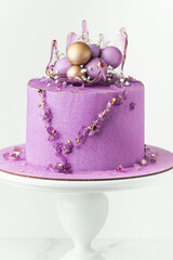 Wedding cake with violet cream cheese frosting decorated with caramel vase and golden chocolate spheres on the white background. Luxury anniversary cake on the white cake stand