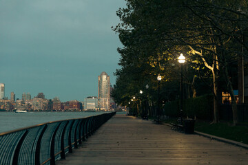 Obraz premium luminous lanterns near trees on Hudson river embankment and evening cityscape of Manhattan in New York City.