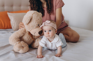Mother playing with teddy bear and baby on bed