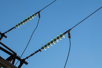 High voltage electric transmission line with glass insulators close-up on blue sky background