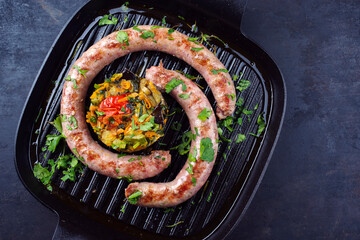 Traditionell gebratene italienische Fleischwurst Salsiccia fresco mit Gemüsetartar und Koriander serviert als Draufsicht in einer gusseisernen Pfanne mit Textfreiraum