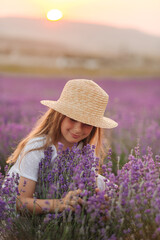 Summer portrait of a beautiful lovely kid girl wearing yellow dress and straw hat in lavender field. she sits and enjoys the scent during sunset. aromatherapy and happy summer in countryside concept
