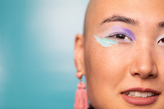 Stylish Gen Z woman wearing colorful makeup in front of blue backdrop
