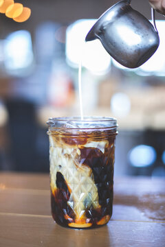 Iced coffee in a tall glass with cream poured over. Cold black coffee with ice cubes in a high glass pour cream.