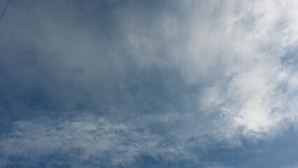rays of the sun through the cirrus clouds against the blue sky, white rainy clouds blue sky illuminated by the rays of the sun, one small cirrus cloud blurred clouds background