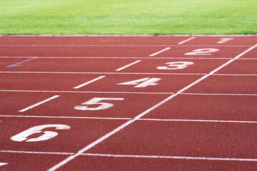 Red running racetrack finishing line with numbers 1-6. Green grass. Landscape or horizontal photo.