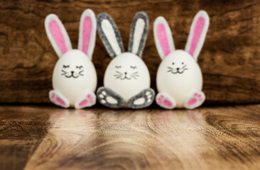 Three defocused Easter eggs with bunny ears on wooden background. Easter concept