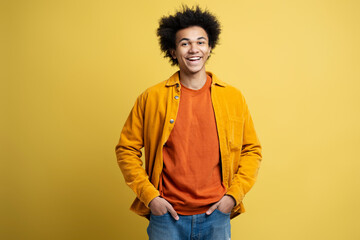 Smiling confident African American man with  wearing stylish casual outfit isolated on yellow background. Happy fashion model holding hands in pockets looking at camera, studio shot 