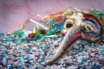 Venetian 'plague doctor' mask with trumpet confetti and streamers around against a pink background