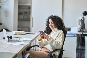 Young happy hispanic business woman office worker looking at smartphone using mobile cell phone...