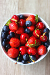 Bowl filled with fresh blueberries, cherries and strawberries on wooden table. Top view. 