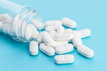 White medicine pills spilling from a container on blue background