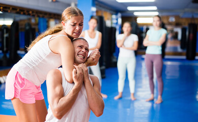 Obraz na płótnie Canvas Young woman performing chokehold movement on man during group self-defence training.