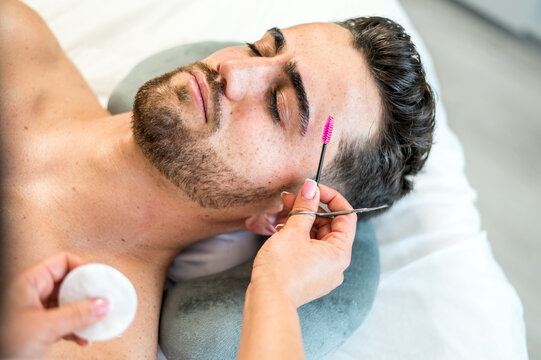 Crop beautician brushing eyebrows of male client