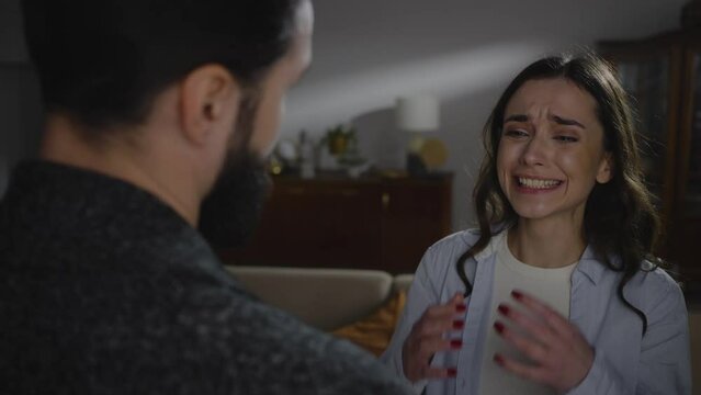 View from the back to a handsome bearded man hugging and consoling a crying offended woman