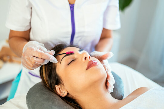 Crop beautician brushing eyebrows of female client