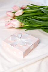Top view of a bouquet of fresh pink tulips and a gift box on the bed in the morning. Gift for valentine's day or women's day