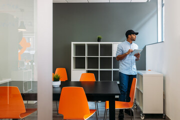 Young thoughtful casual employee surfing internet on tablet in office