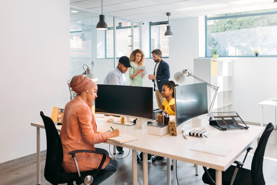 Multi coworkers speaking at table with computers in office